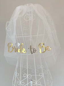 Slöja till möhippan med texten “Bride to be”. Vitt tyll med printad text i guld.